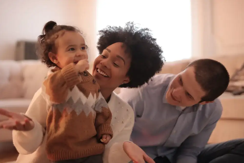 Mãe, pai e dois filhos pequenos sentados juntos na sala de casa