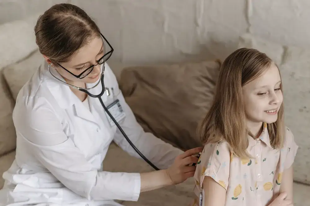Pediatra sorrindo enquanto examina uma menina em consultório claro e acolhedor